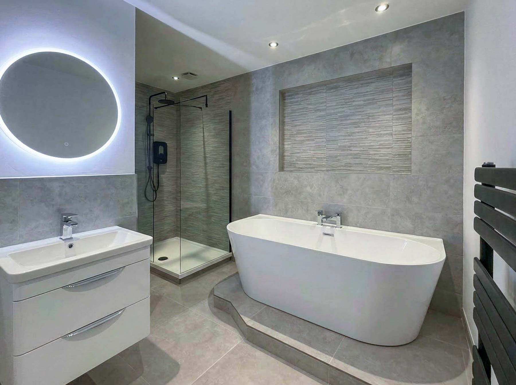 Modern bathroom with freestanding bathtub, walk-in glass shower, illuminated round mirror, and white vanity unit